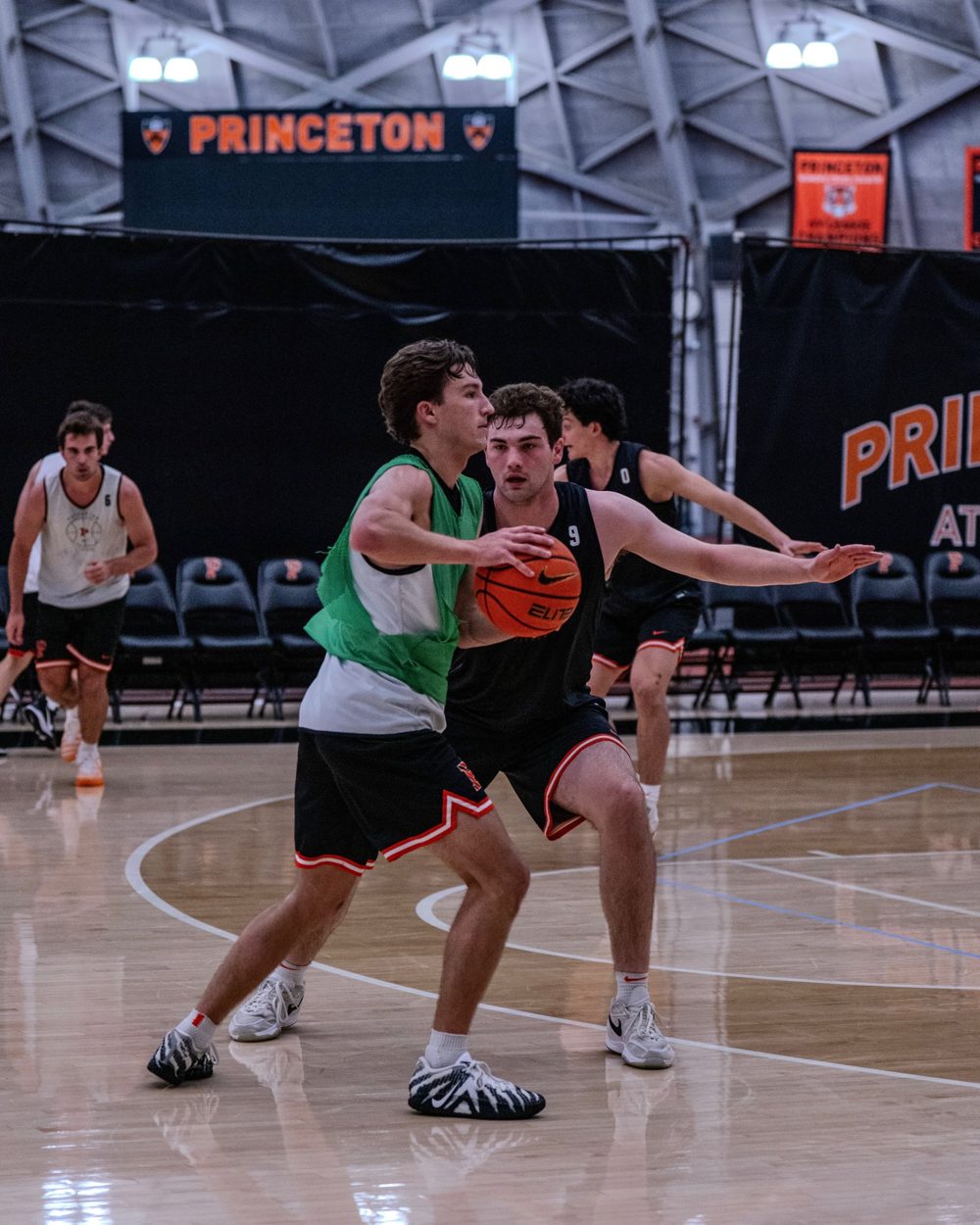 A guard in a green pinnie is guarded by a teammate in a half-court drill