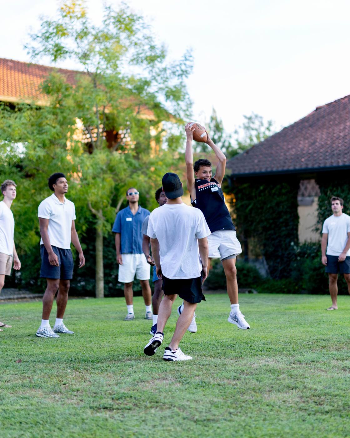 A player jumps to catch a football on the lawn while others watch