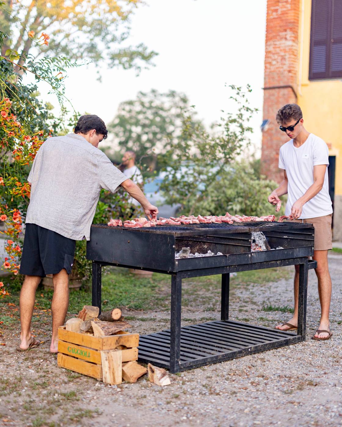 Two people arranging meat on a wood-fired grill