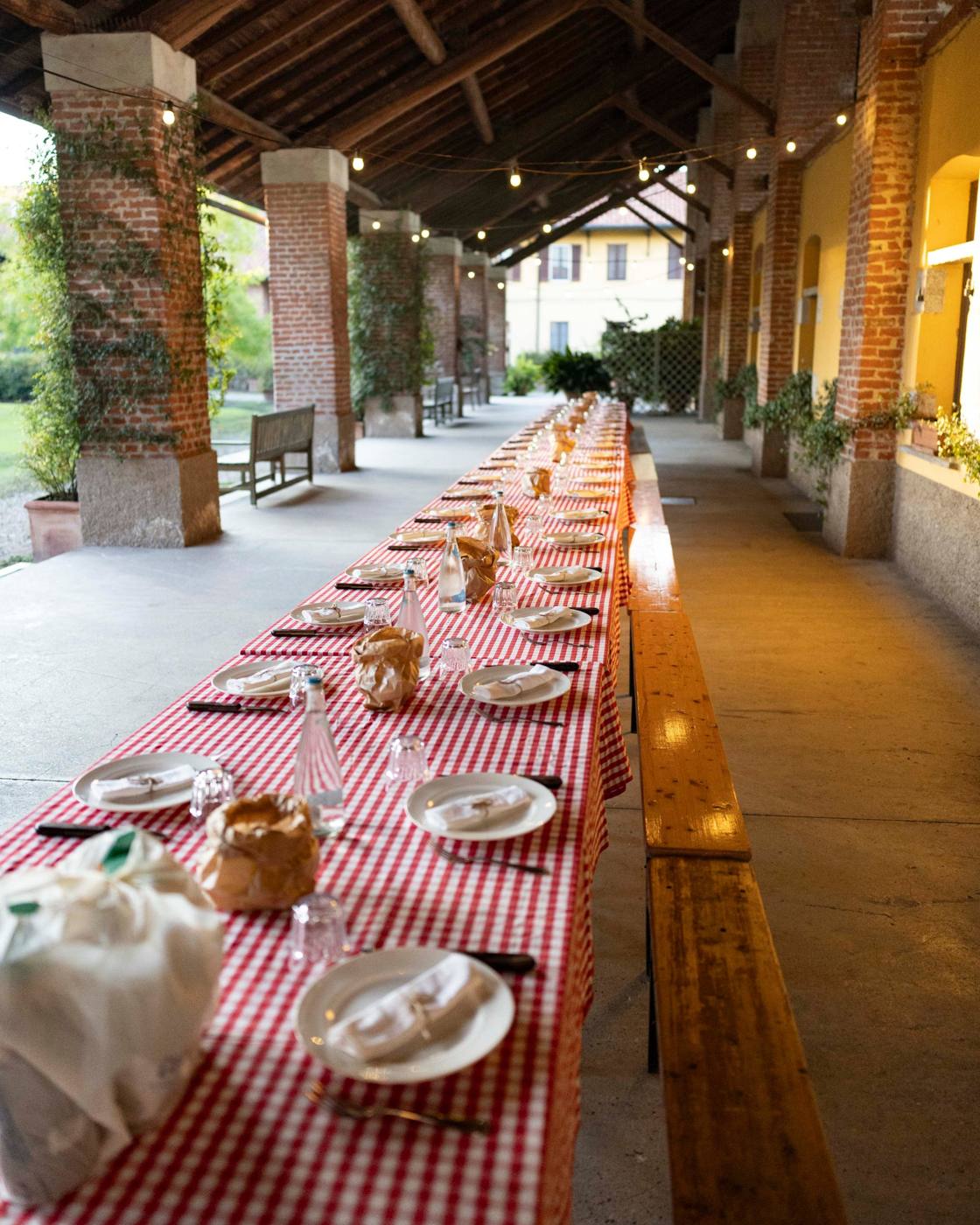 A long table set with plates and a red-and-white checked cloth beneath a covered terrace